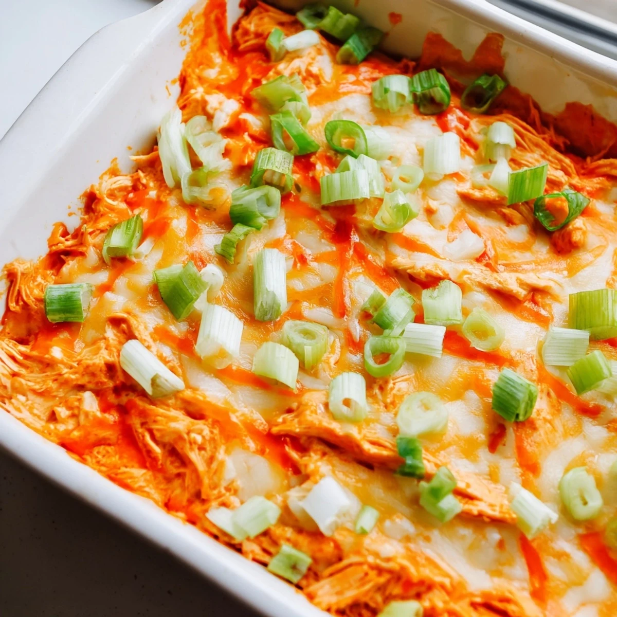 Golden, creamy spicy Buffalo chicken dip served in a baking dish with ranch drizzle and a side of crunchy vegetables.