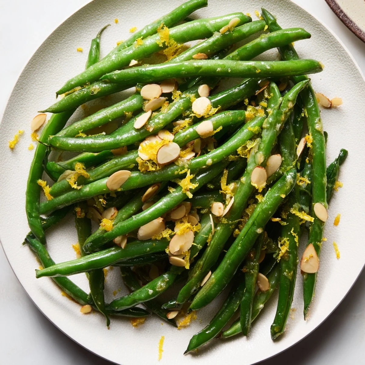 Bright green beans with lemon and almonds topped with extra toasted almonds on a rustic wooden board.