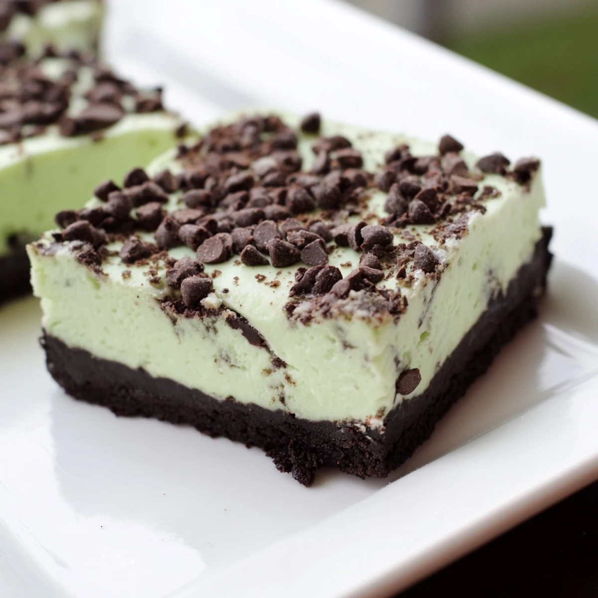Freshly cut Mint Chocolate Chip Cheesecake Bars reveal a creamy, mint-green filling packed with chocolate chips atop a dark cookie crust. 