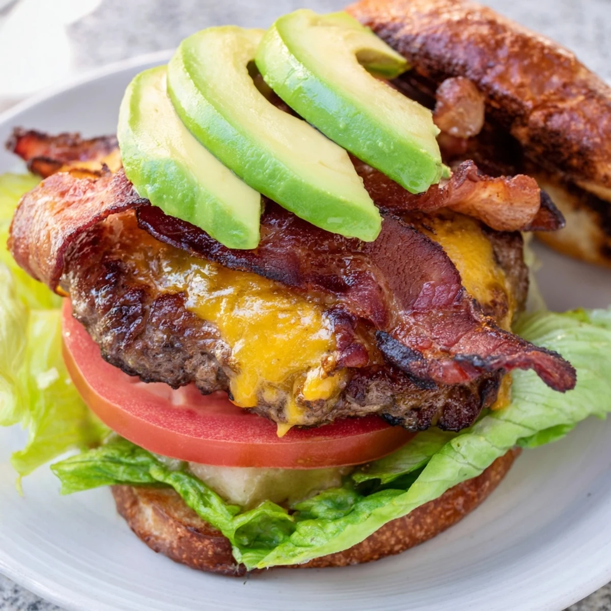 A close-up view of a juicy beef burger with creamy avocado and smoky bacon layers.