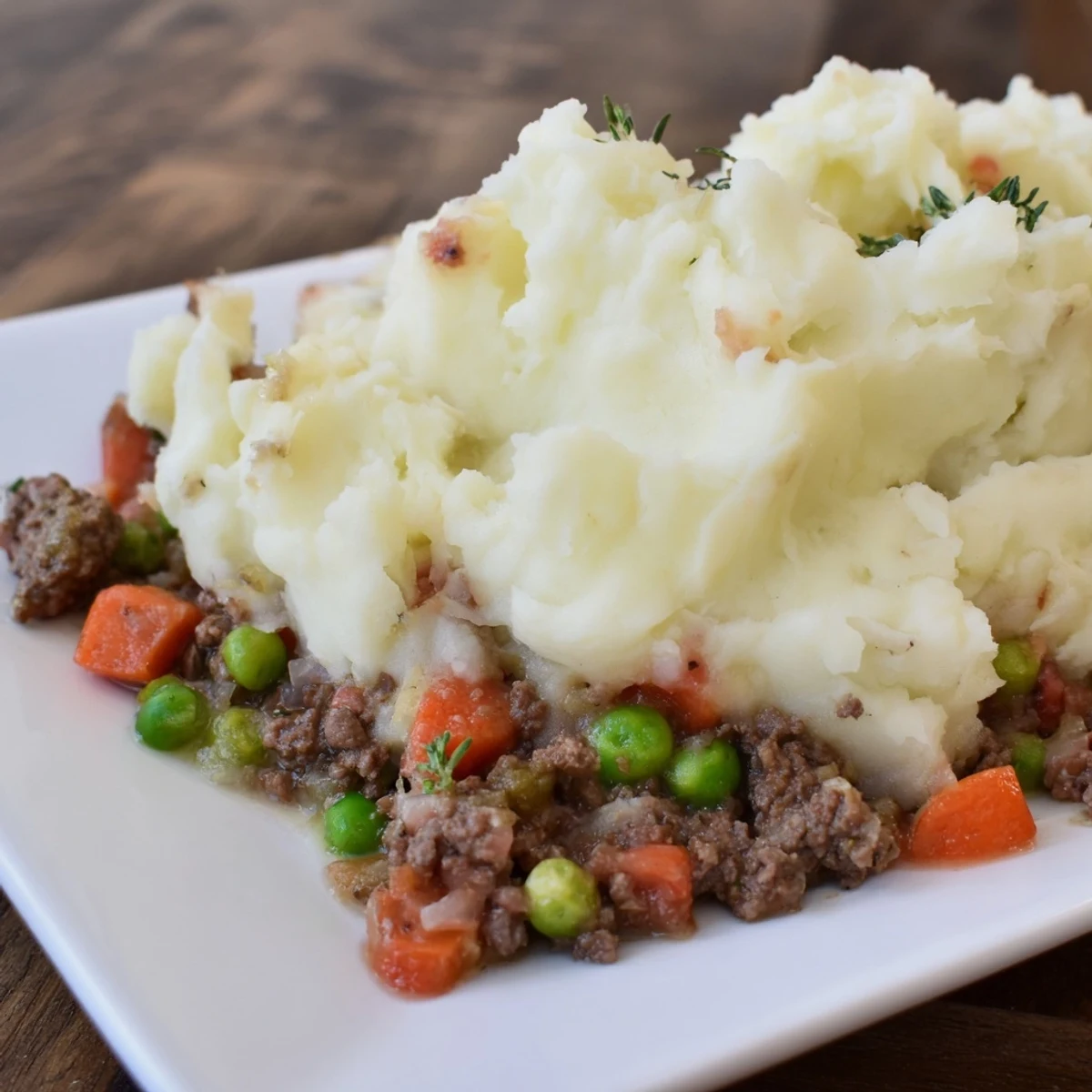 Steam rises from a hearty serving of Beef Shepherds Pie with Peas on a rustic dinner plate.
