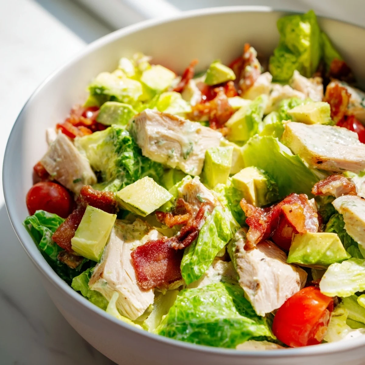 A close-up view of BLT Chicken Salad, featuring sliced avocado and fresh chives on a white plate.