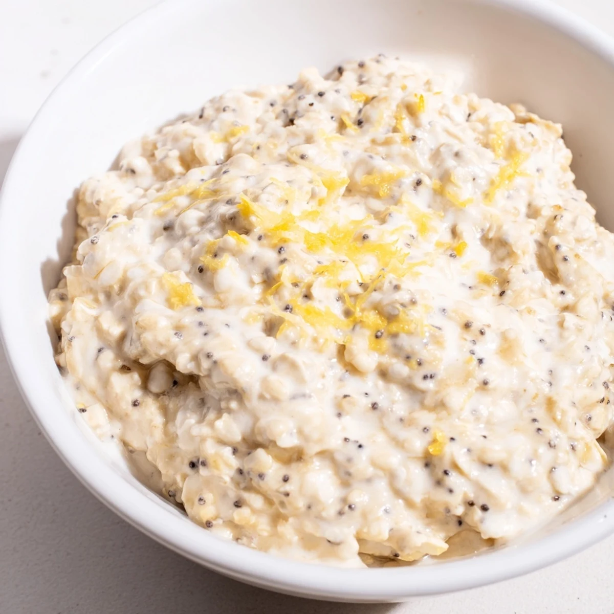 A close-up of vegan lemon poppy seed overnight oats with coconut yogurt and a lemon zest garnish.