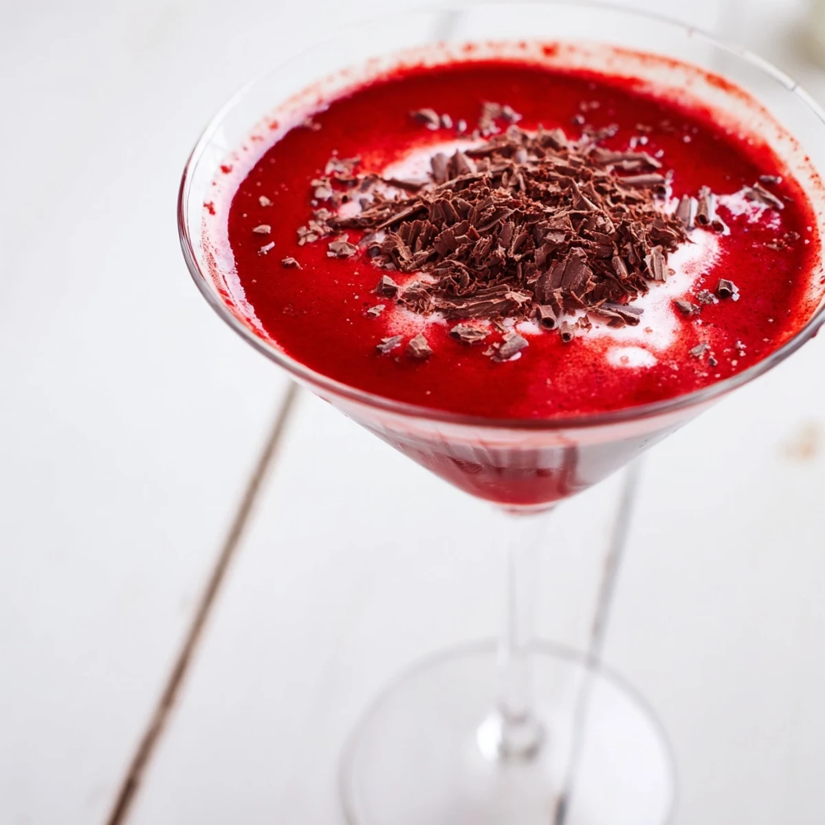 A close-up of Decadent Red Velvet Martini garnished with chocolate shavings and cream cheese frosting on the rim.