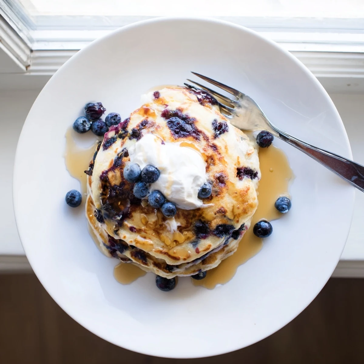 Golden Fluffy Greek Yogurt Blueberry Pancakes topped with fresh blueberries and a dollop of yogurt.