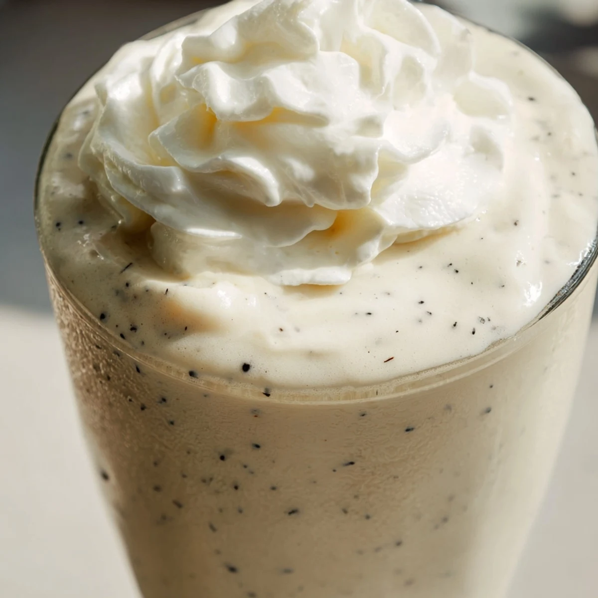 A tall glass of Starbucks Vanilla Bean Frappuccino topped with fluffy whipped cream, a refreshing creamy treat.