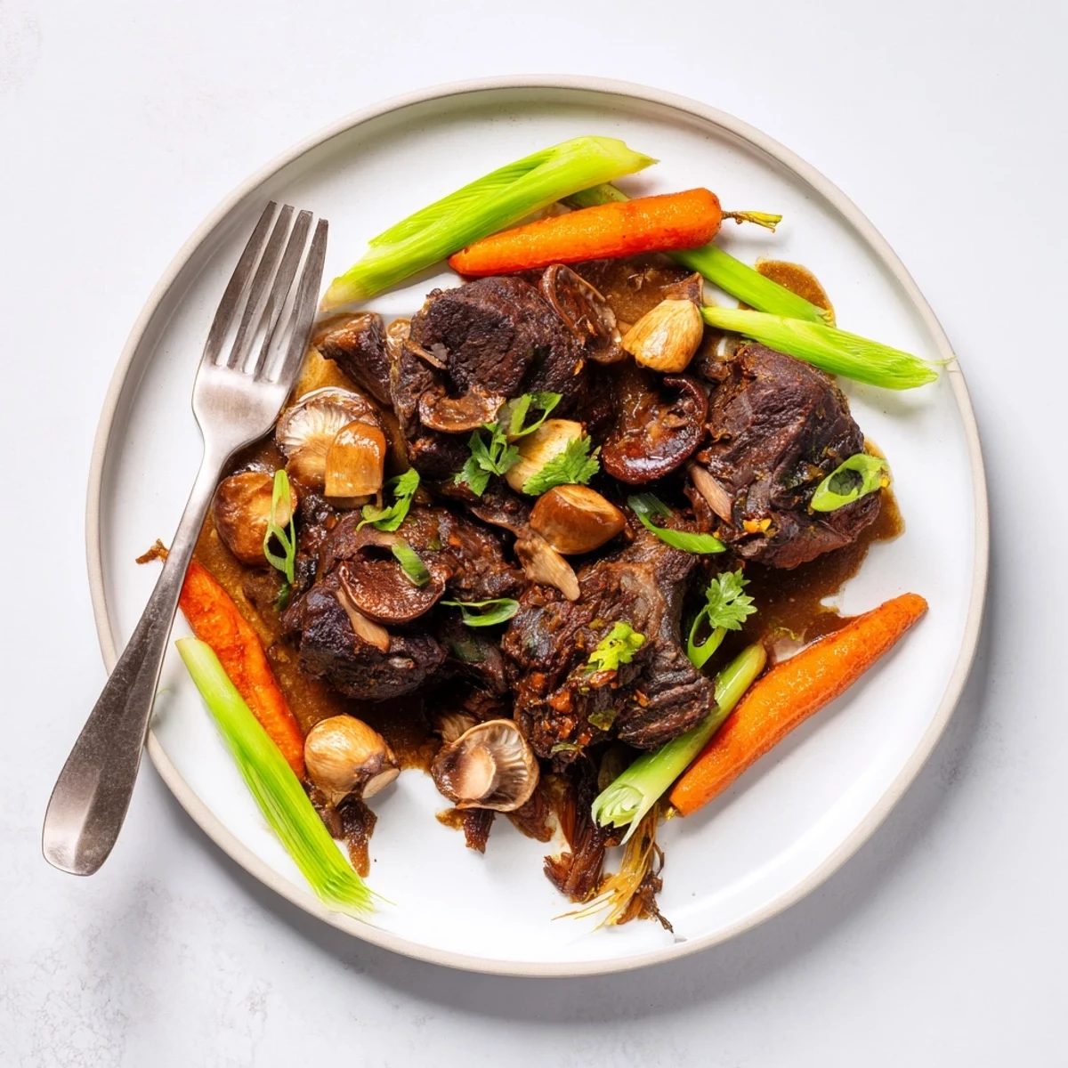 A close-up of glazed Asian Style Slow Cooked Beef Cheeks With Mushrooms, garnished with scallions and fresh cilantro.