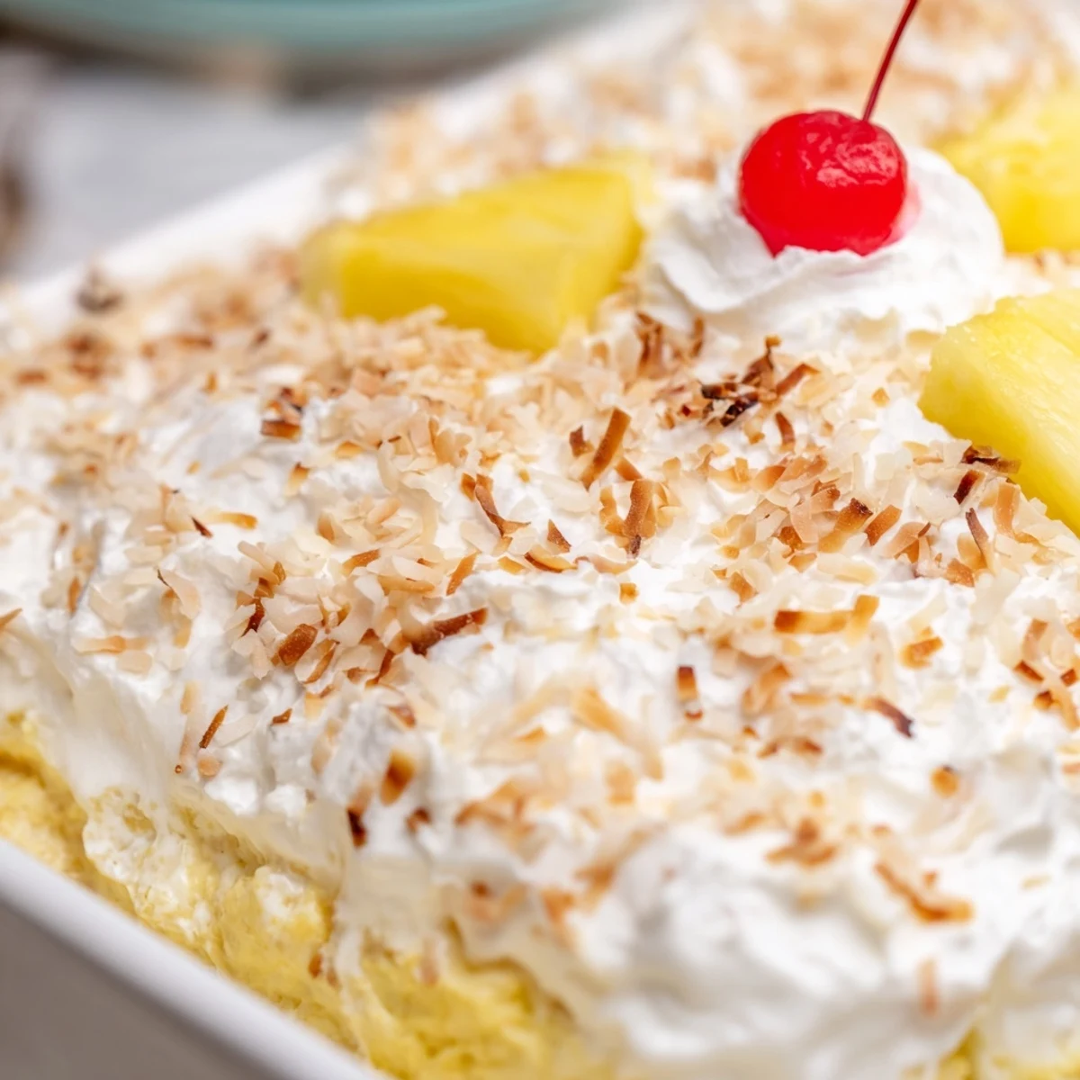 Hawaiian poke cake topped with fluffy whipped cream and golden toasted coconut flakes