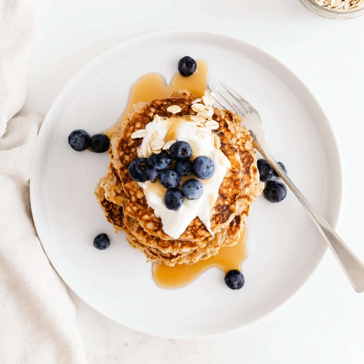 Golden stack of fluffy banana oatmeal pancakes topped with creamy Greek yogurt and maple syrup