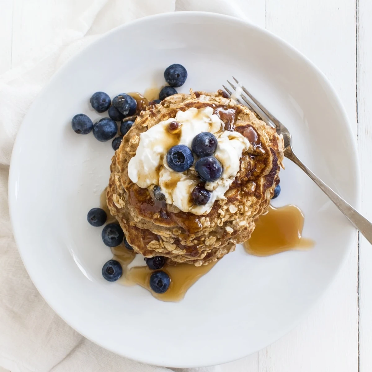 Warm banana oatmeal pancakes drizzled with syrup and garnished with Greek yogurt and sliced banana