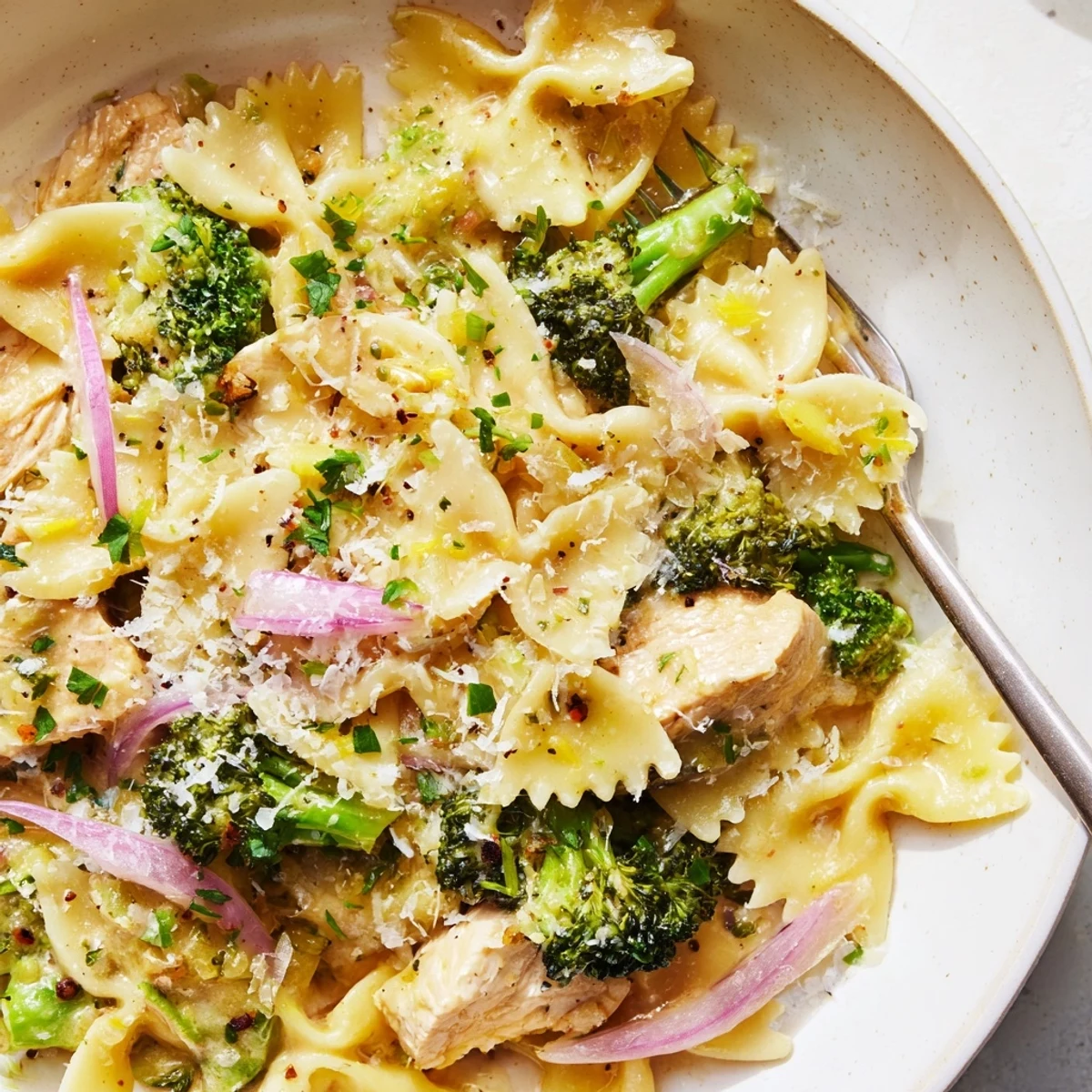 Golden brown chicken pieces and bright green broccoli florets tossed with bowtie pasta in a creamy lemon butter sauce topped with grated Parmesan cheese