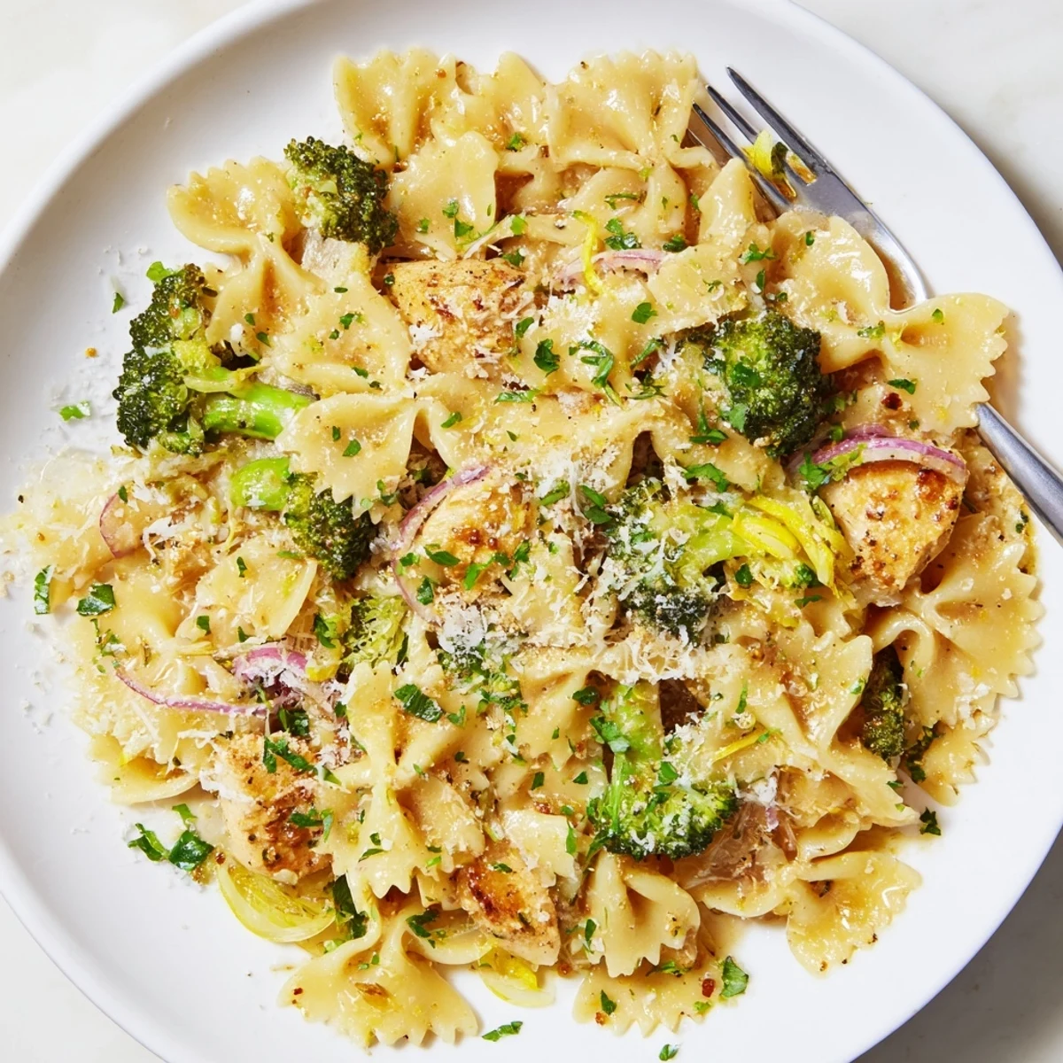 Steamy bowl of cowboy butter lemon pasta featuring tender chicken breast crisp broccoli and farfalle noodles garnished with fresh parsley and chives