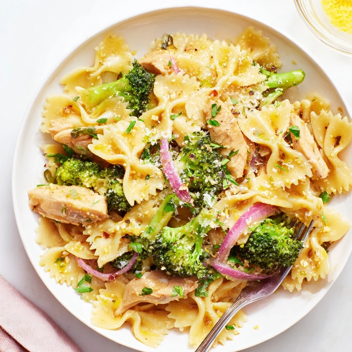 Weeknight dinner plate loaded with zesty cowboy butter lemon bowtie pasta with chunks of juicy chicken and tender broccoli sprinkled with Parmesan