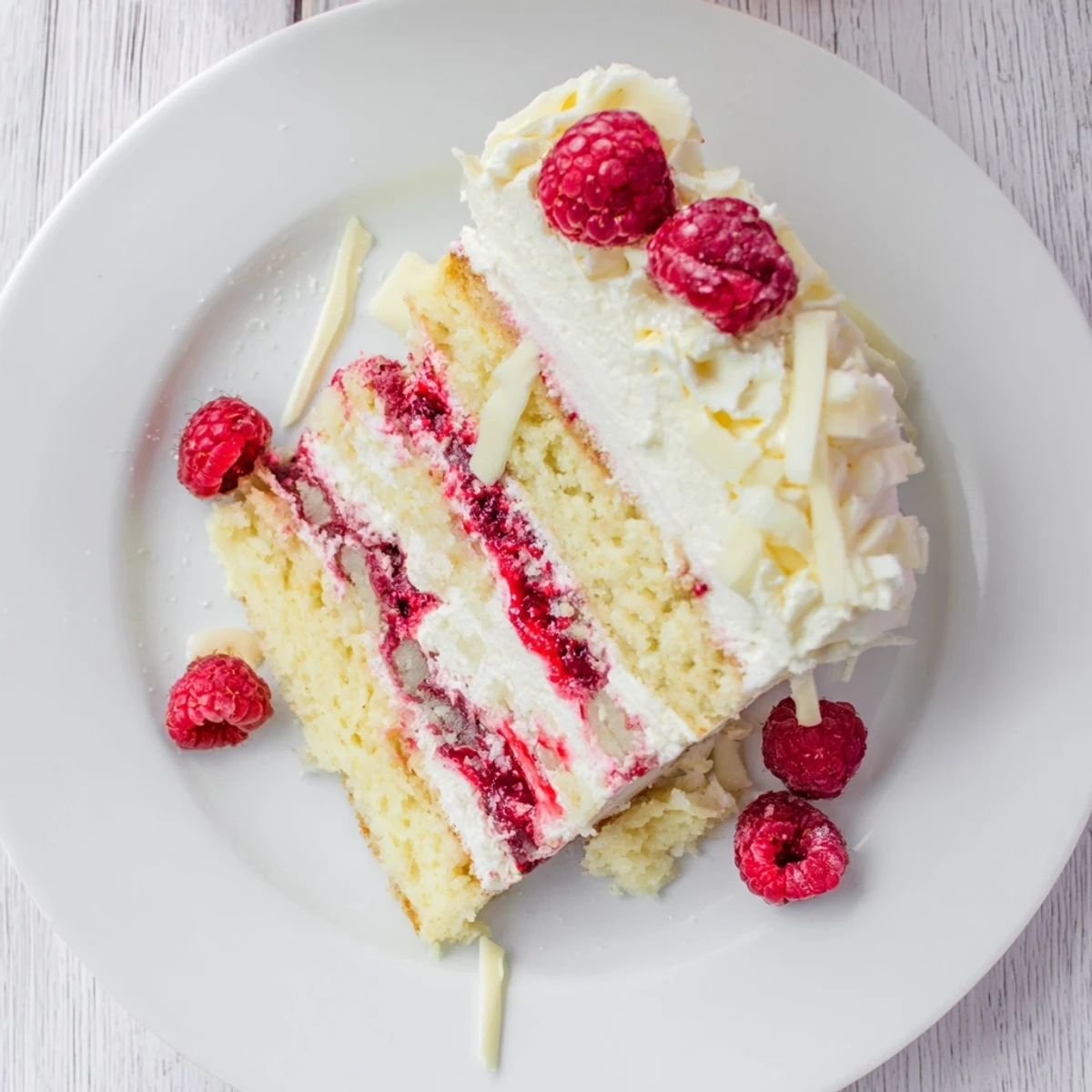 Decadent white chocolate raspberry cream cake garnished with fresh raspberries and white chocolate curls