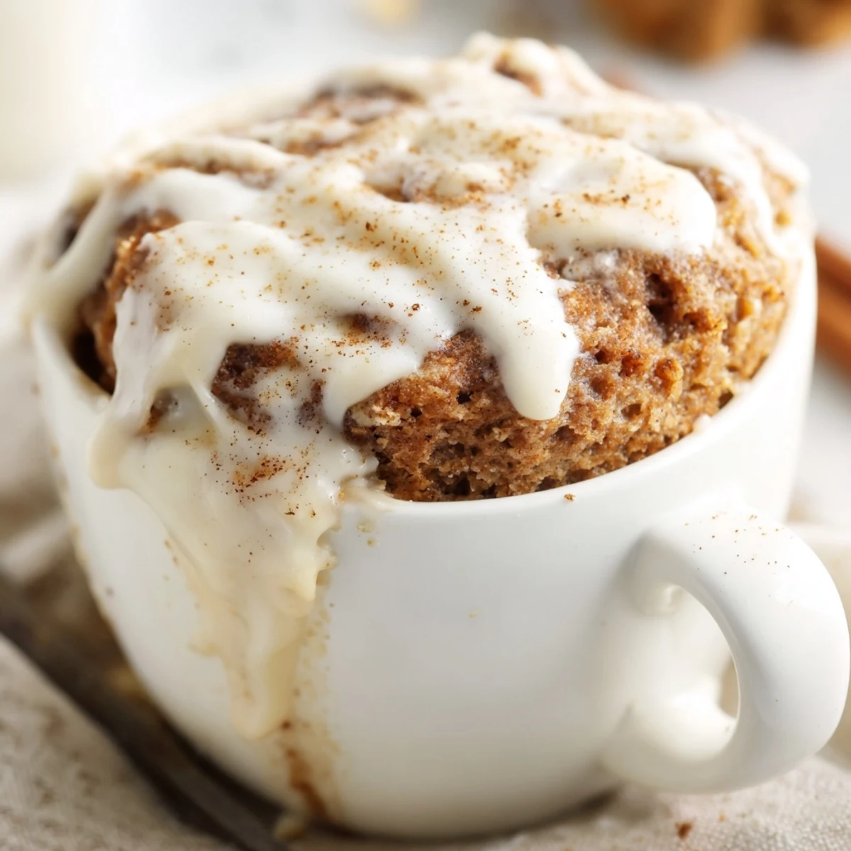 Protein-packed cinnamon roll mug cake topped with creamy vanilla icing in a microwave-safe vessel
