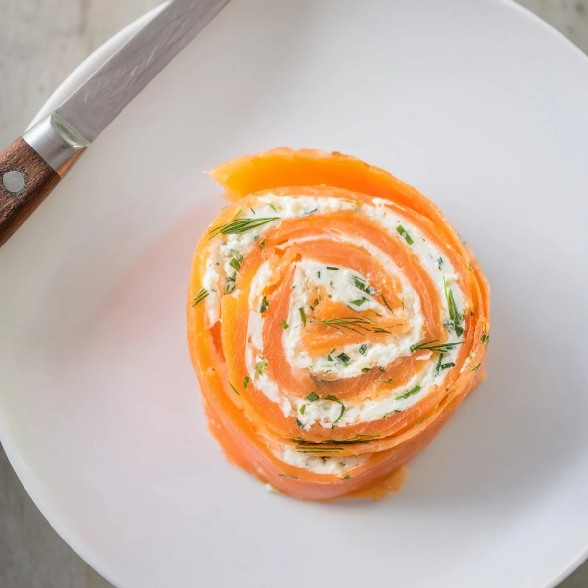 Close-up of smoked salmon roll ups arranged on a wooden board with dill garnish and cream cheese center visible