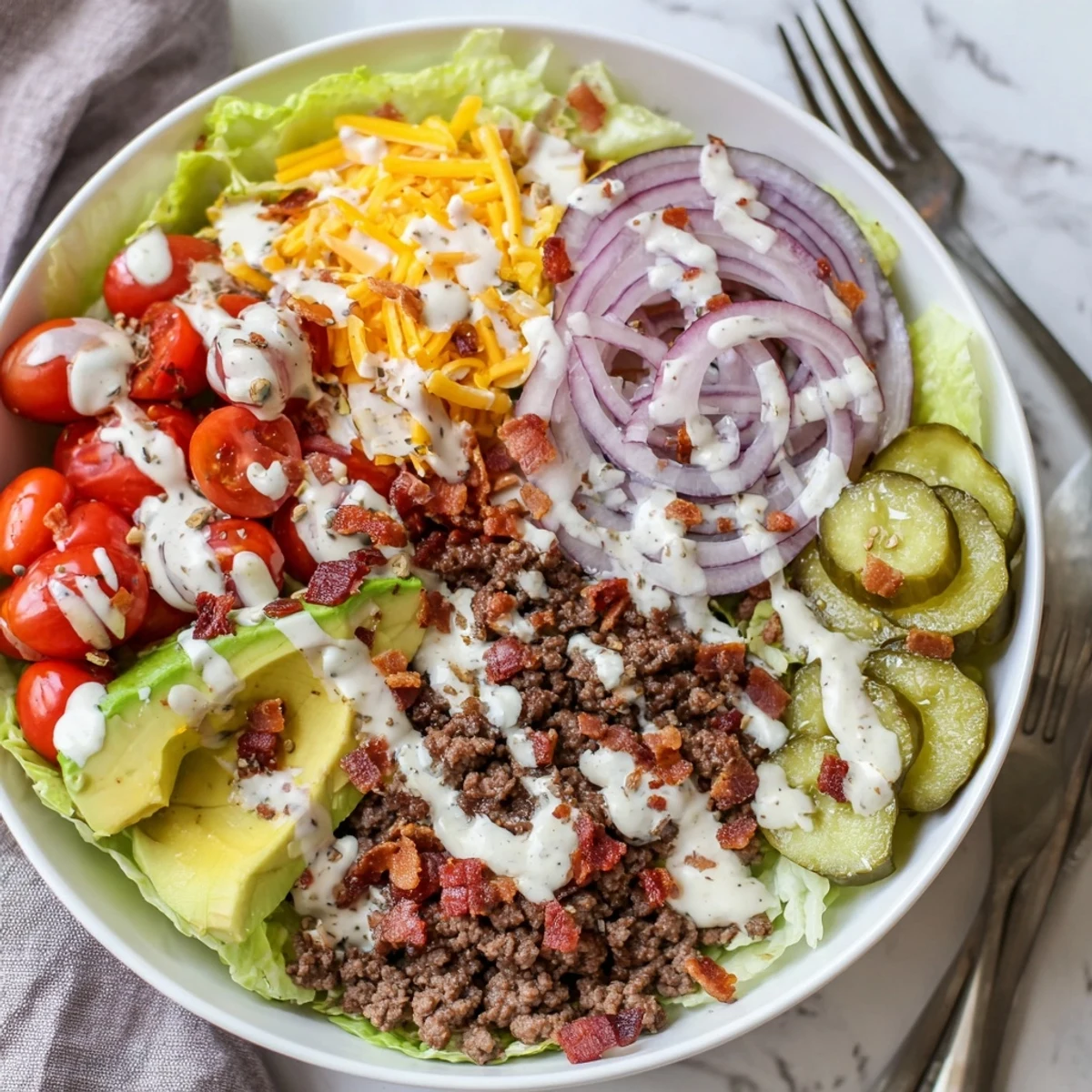 Low-carb burger bowl featuring seasoned beef, melted cheddar, fresh veggies, and creamy dressing.