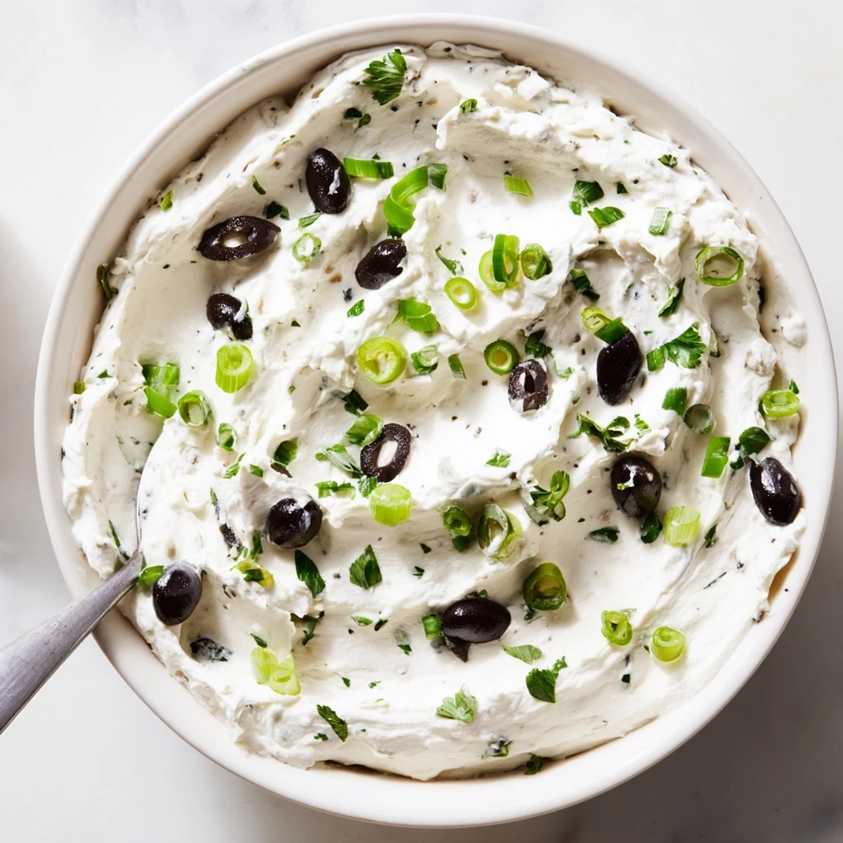 Cream cheese olive dip with chopped green and black olives in white serving bowl