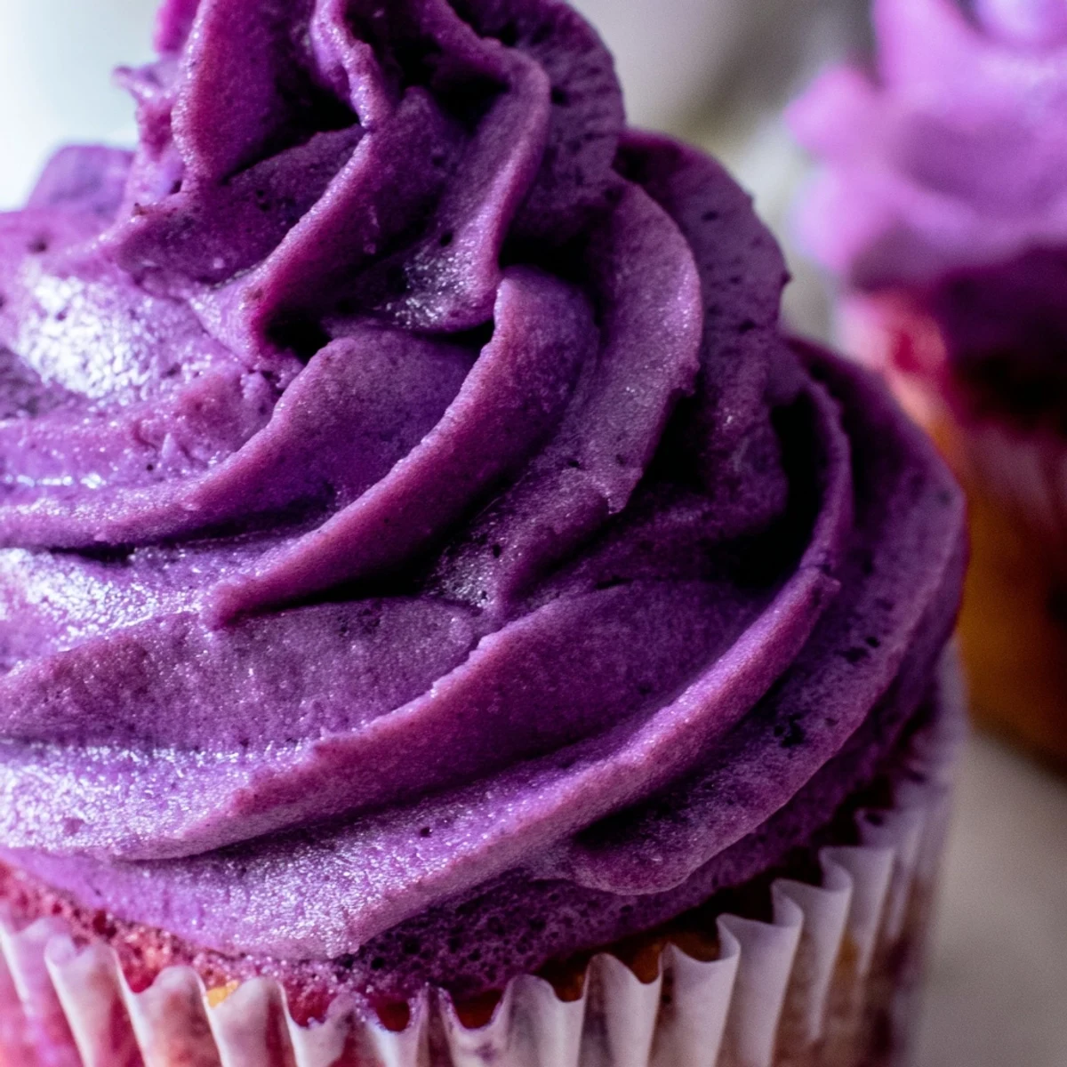 Fluffy grape soda cupcakes topped with smooth purple grape buttercream frosting on a white plate