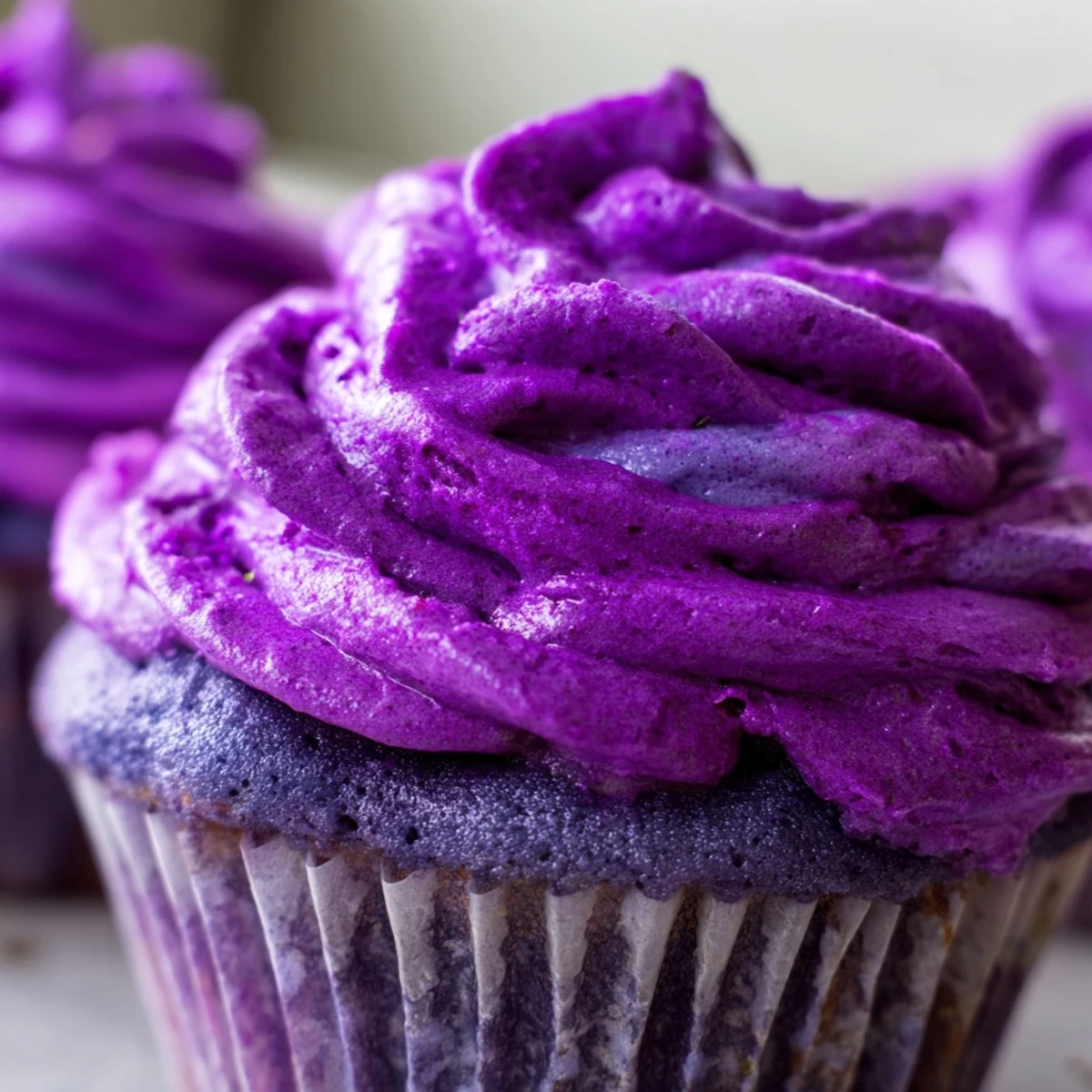 Homemade grape soda cupcakes with fluffy grape buttercream sitting in paper liners on a wire rack