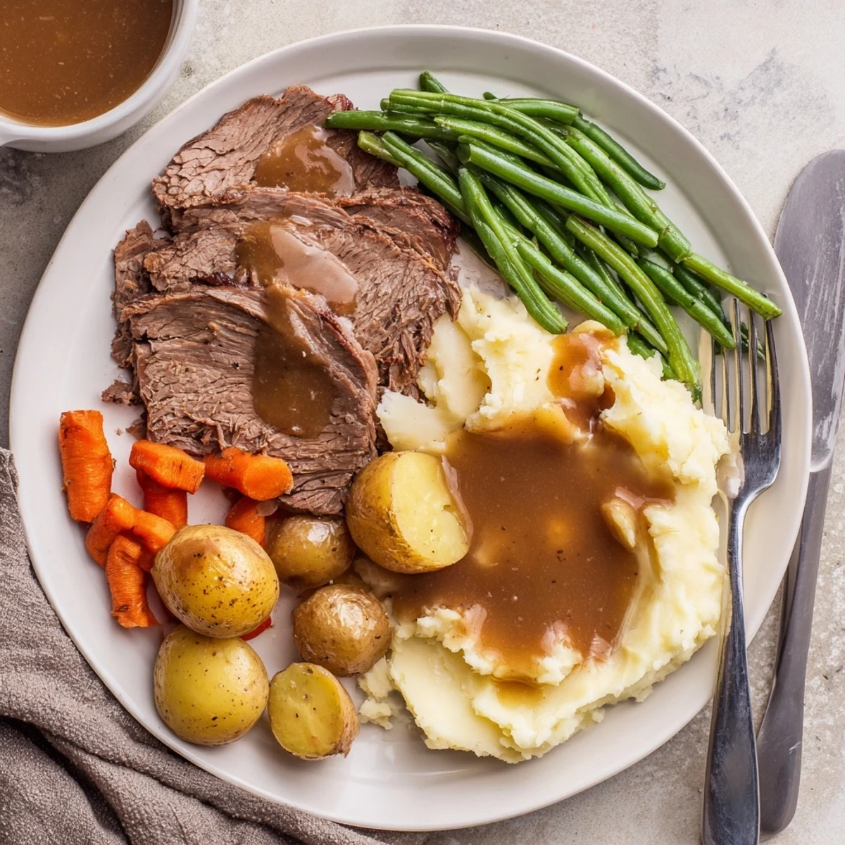 Tender Southern style pot roast with rich gravy served beside fluffy mashed potatoes and buttery green beans on a white dinner plate