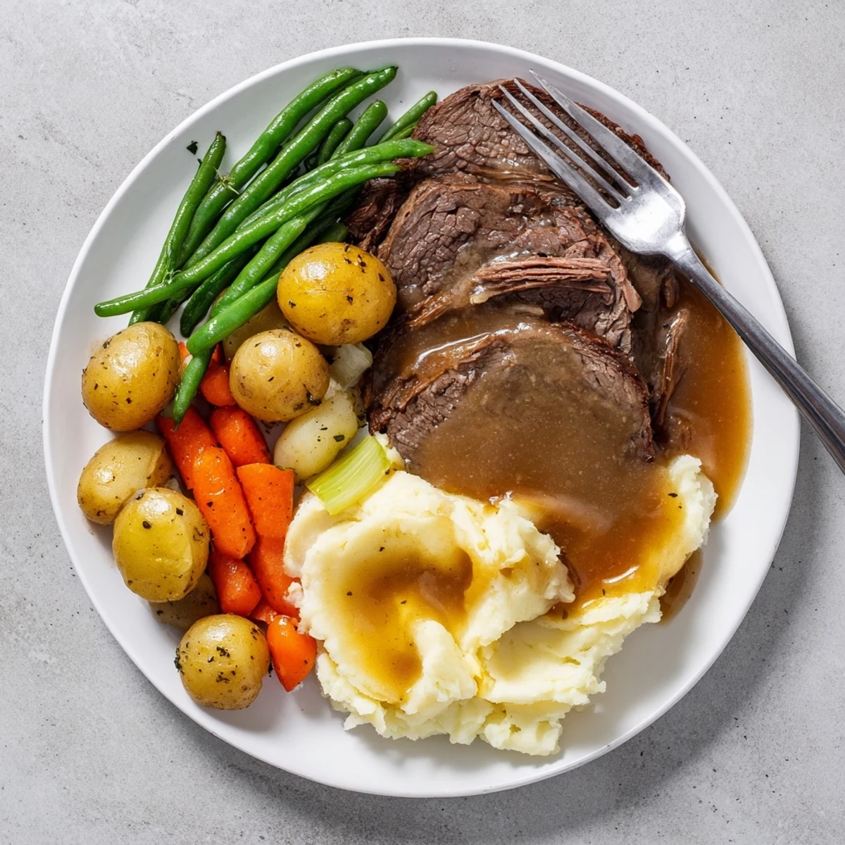 Fork-shredded beef Southern style pot roast plated with roasted vegetables, creamy potatoes, and fresh seasoned green beans for a hearty Sunday supper