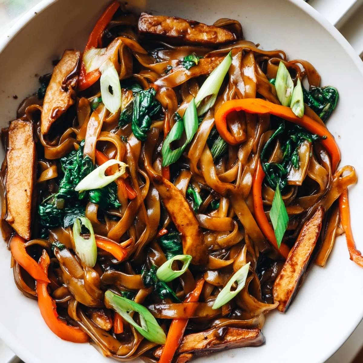 Steaming plate of vegan pad see ew featuring wide noodles, Chinese broccoli, and marinated tofu strips