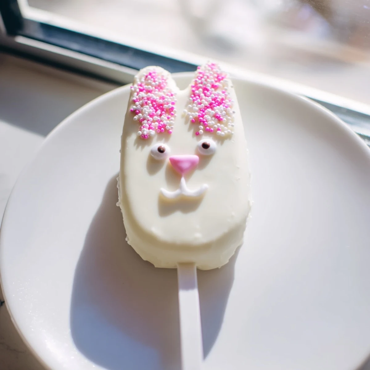 Creamy white chocolate bunny cakesicles decorated with sprinkles and fondant ears for spring celebrations