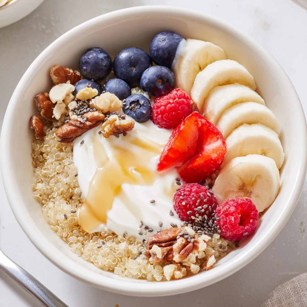 Creamy yogurt-topped Quinoa Breakfast Bowl drizzled with honey and toasted coconut.