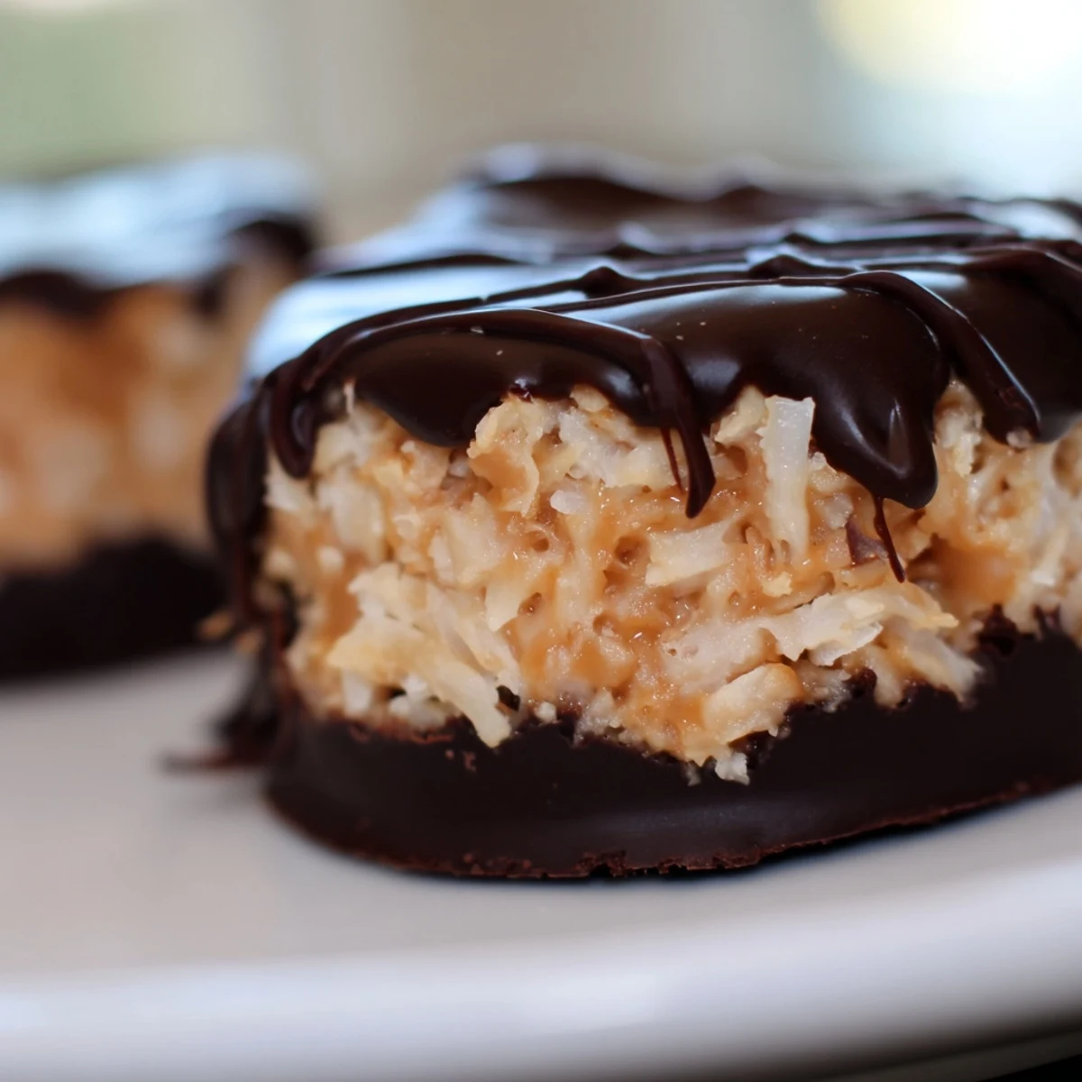 No bake Samoa bites featuring chocolate drizzled coconut and caramel stacked on a dark plate