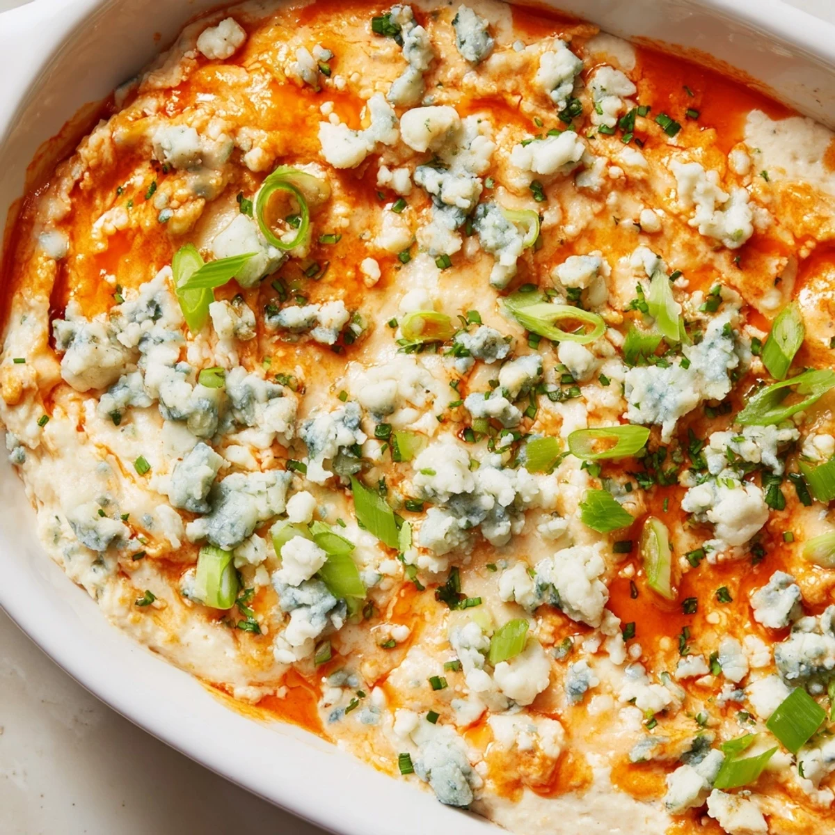 Golden white bean buffalo dip bubbling with melted cheddar and blue cheese crumbles, topped with fresh green onions