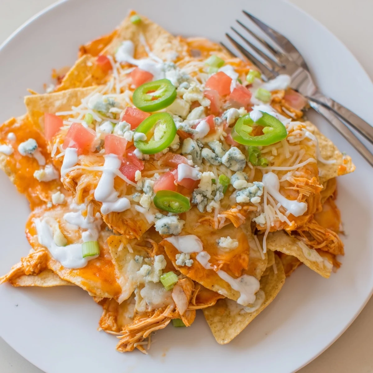 Buffalo Chicken Nachos piled with melty cheddar, spicy chicken, scallions, and ranch drizzle
