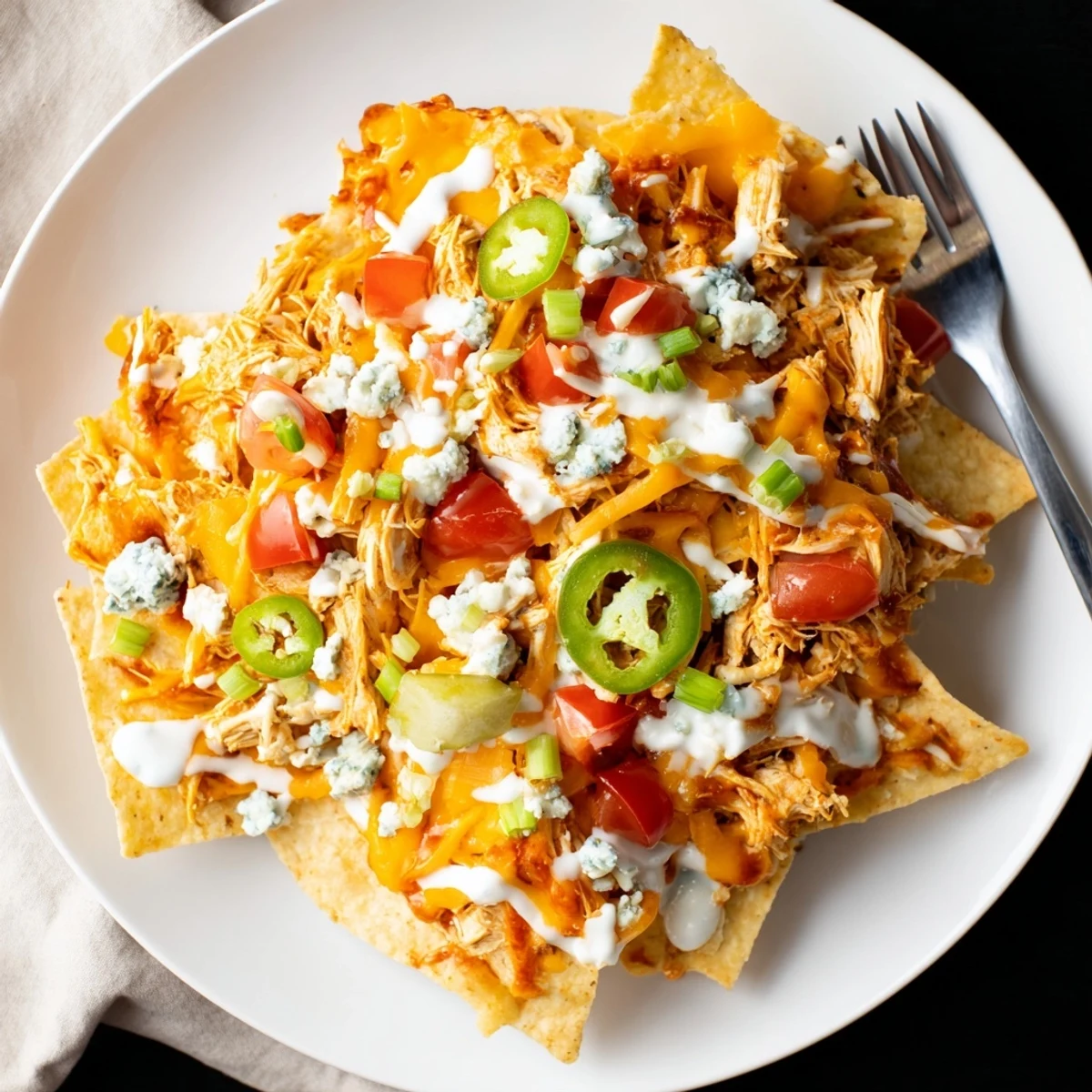 Party ready Buffalo Chicken Nachos layered on a platter, tomatoes, blue cheese crumbles