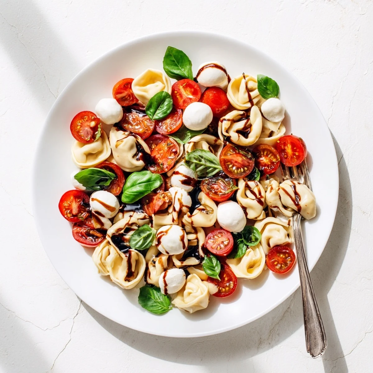 Colorful Tortellini Caprese Salad with cherry tomatoes, fresh mozzarella, and basil leaves drizzled with balsamic glaze in a white serving bowl