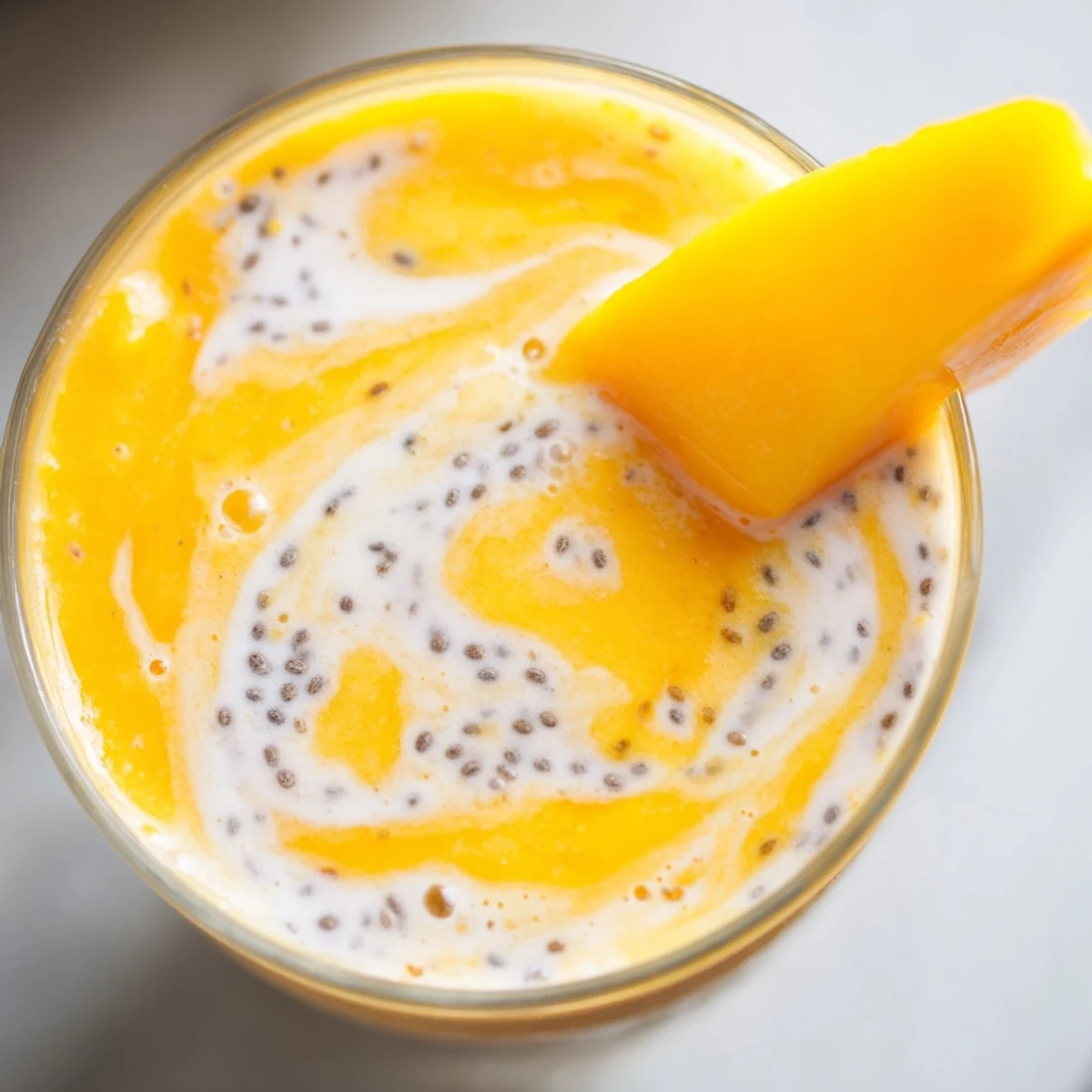 Glass of vibrant Tropical Sunrise Protein Smoothie garnished with fresh mango slice on wooden table